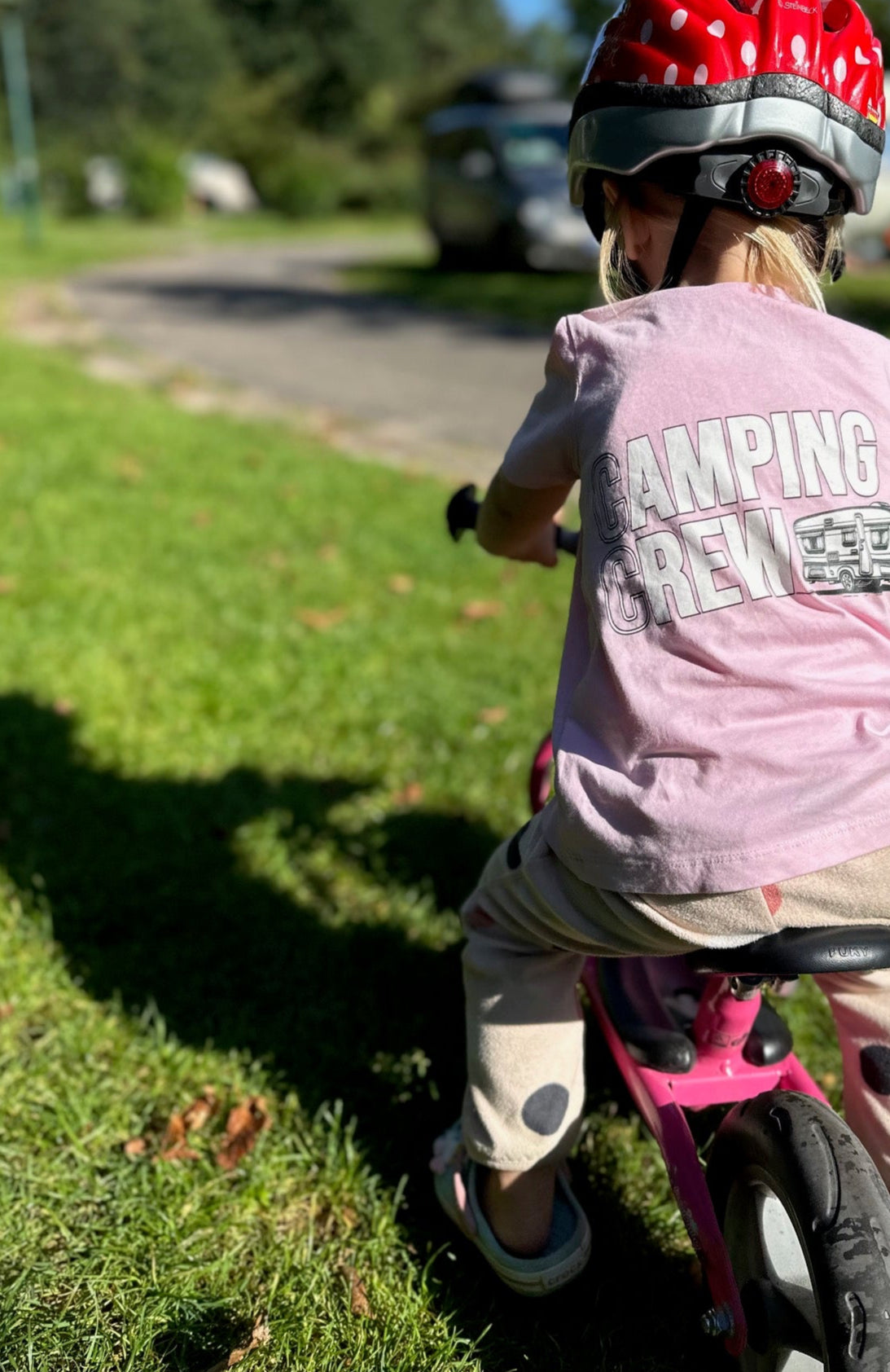 Kind auf dem Laufrad im rosa Camping-Crew-T-Shirt